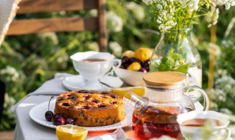 Tavola all'aperto con tè, torta e fiori, atmosfera estiva.