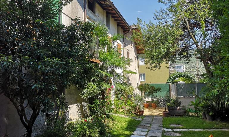 Giardino verde con alberi e sentiero acciottolato accanto a una casa.