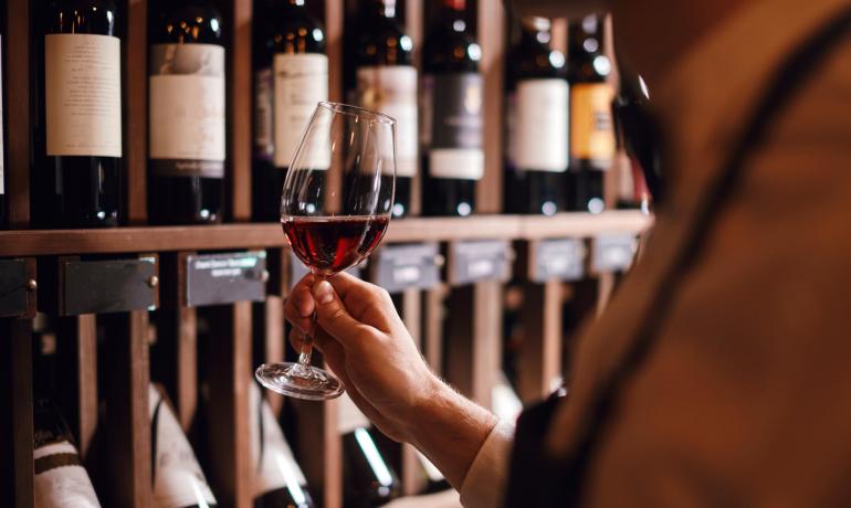 Persona con bicchiere di vino rosso in una cantina.