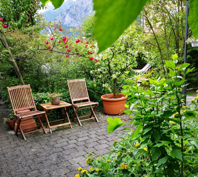 Giardino fiorito con sedie in legno e tavolo su pavimento in pietra.