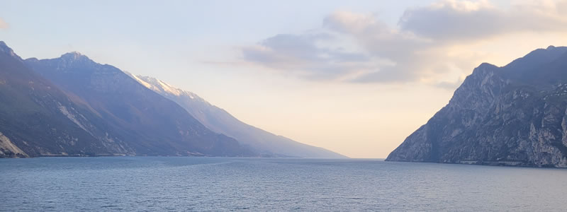 Lago tra montagne al tramonto, cielo nuvoloso.